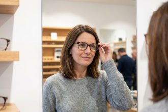 Femme essayant des lunettes modernes dans une opticerie de Sens, ambiance boutique contemporaine