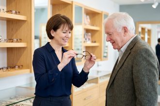 Opticienne aidant un senior à choisir des lunettes dans une boutique